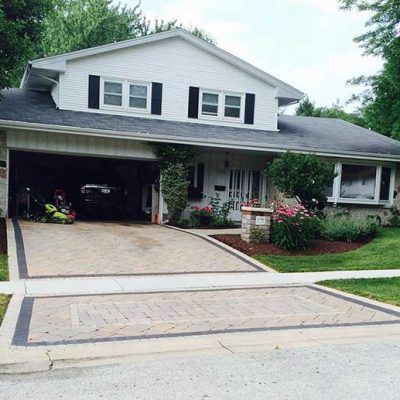 A white house with a driveway and a lawn mower parked in front of it.