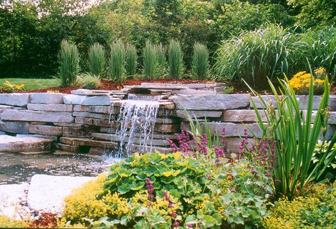 There is a waterfall in the middle of a garden surrounded by flowers.
