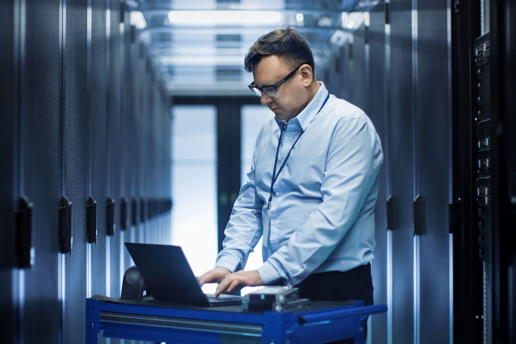 A man is using a laptop computer in a server room.