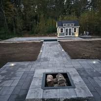A fire pit with logs in it and a house in the background.