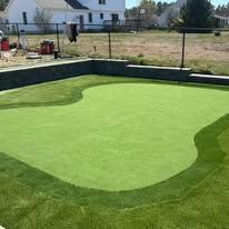 A green putting green in a backyard next to a fence.