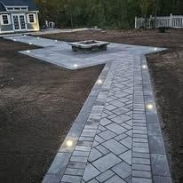A brick walkway leading to a fire pit in a backyard.