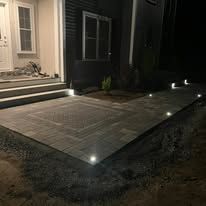 A brick walkway is lit up at night in front of a house.