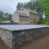 A large brick wall surrounds a swimming pool in front of a house.