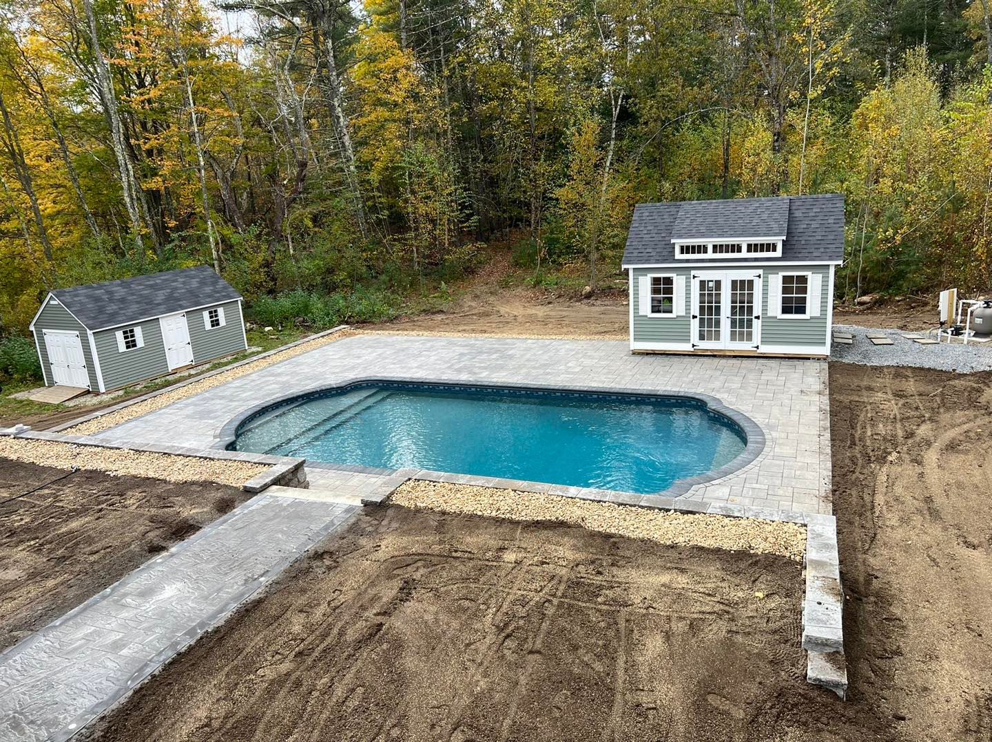 A large swimming pool is surrounded by dirt and a shed.