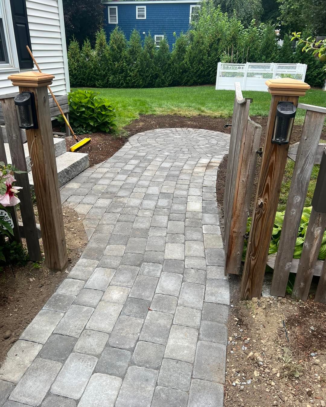 A brick walkway leading to a wooden fence and a blue house.