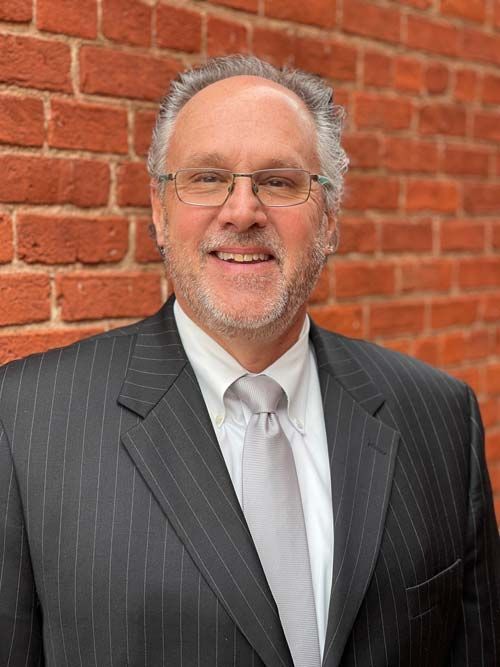 A man in a suit and tie is smiling in front of a brick wall.