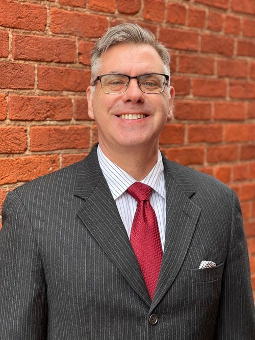 A man in a suit and tie is smiling in front of a brick wall.