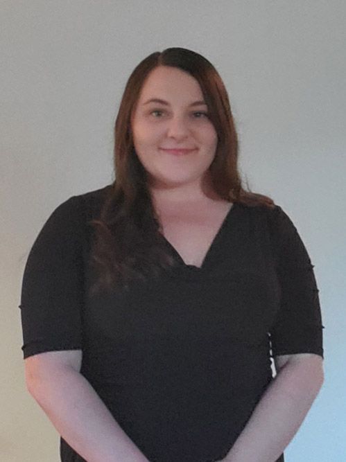A woman in a black shirt is standing in front of a white wall.