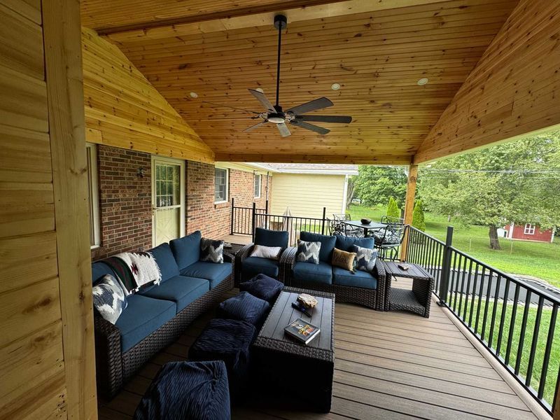 Covered porch with blue furniture, a ceiling fan, and a view of a yard and trees.