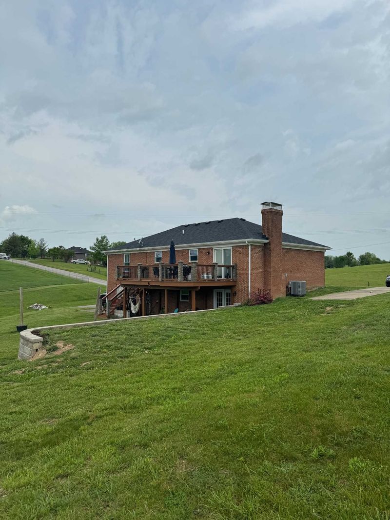 Brick house with deck on grassy hill under cloudy sky.