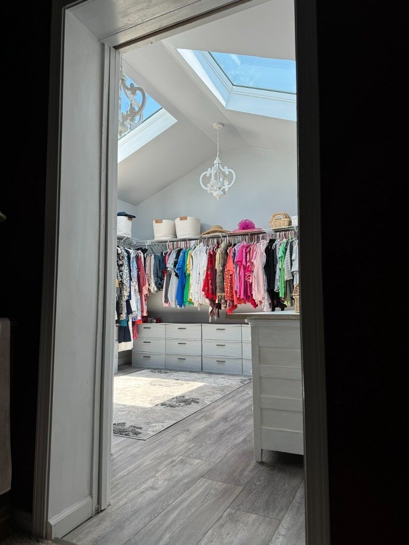 A light-filled walk-in closet with clothes racks, drawers, skylights, and a chandelier.