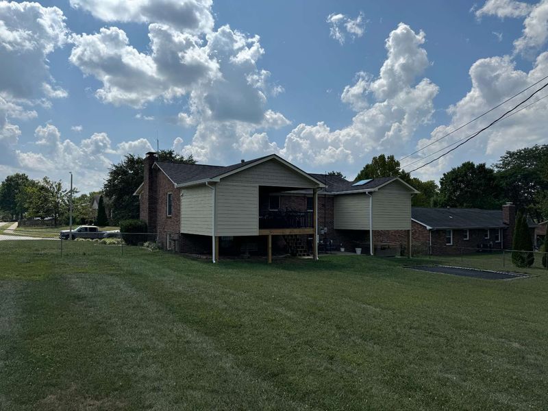 Backyard view of a house with a deck, brick and siding exterior, under a partly cloudy blue sky.