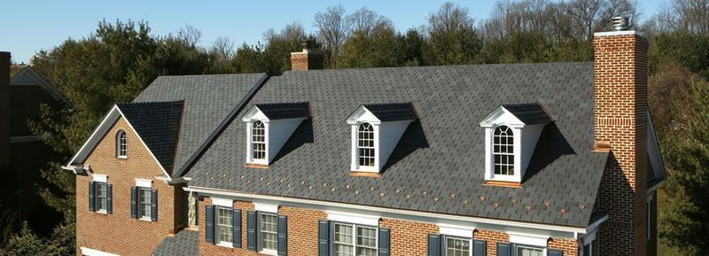 Brick house with gray roof, three dormers, and a tall brick chimney.