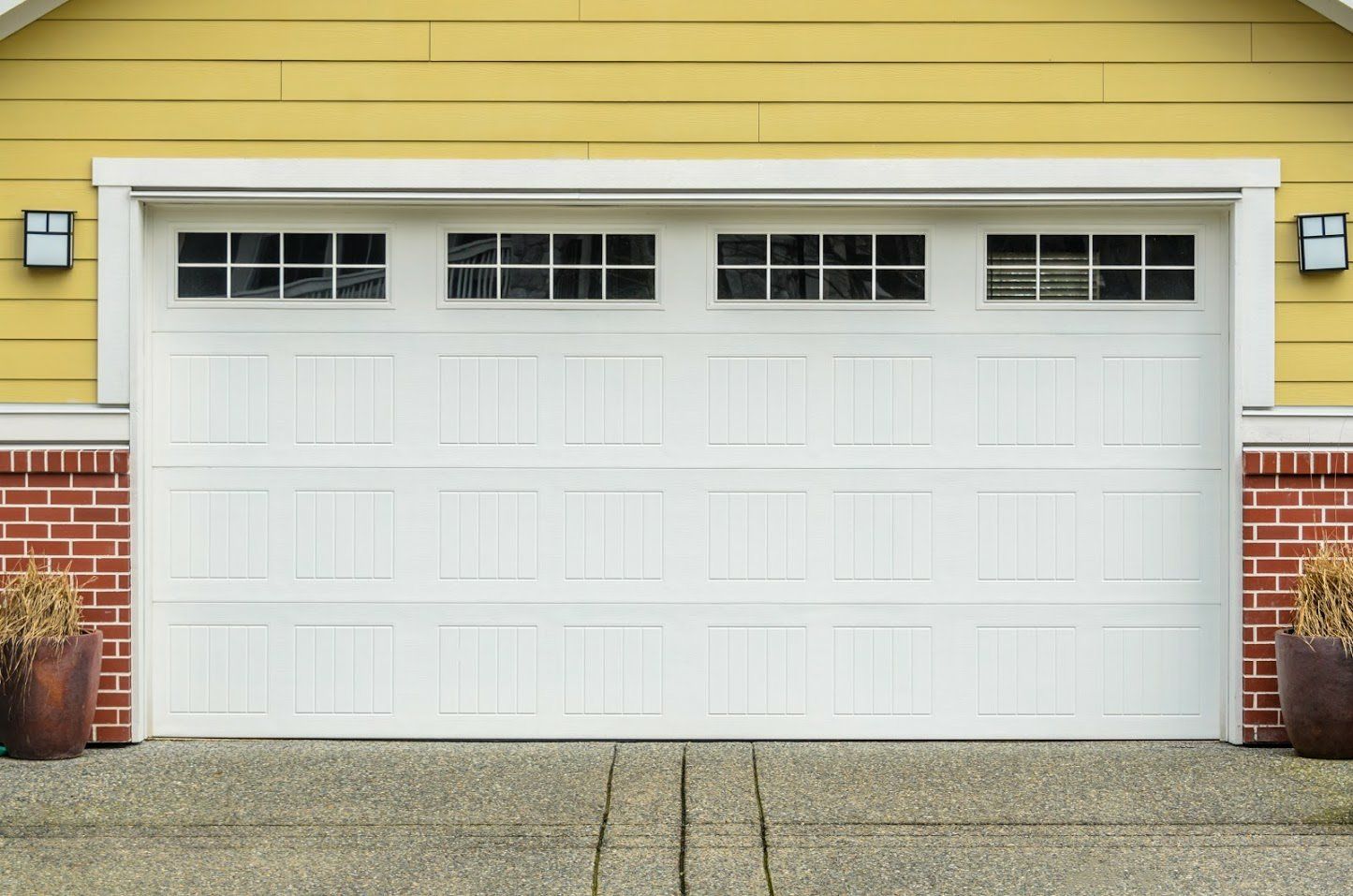 White garage door with windowed top, yellow siding, and brick accents.