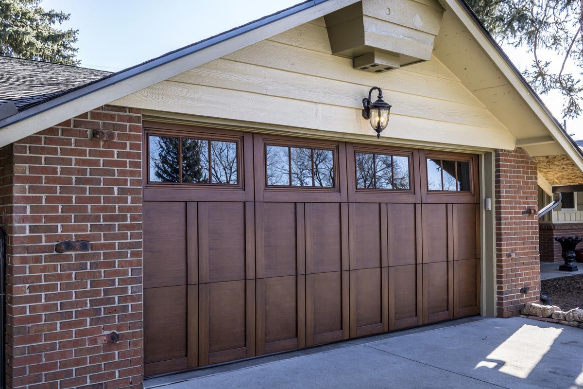 Brown garage door with windows, brick exterior, and decorative light fixture.