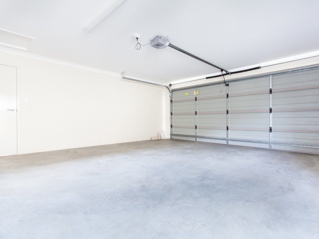 Empty, gray concrete garage with closed, silver garage door. White walls and ceiling.
