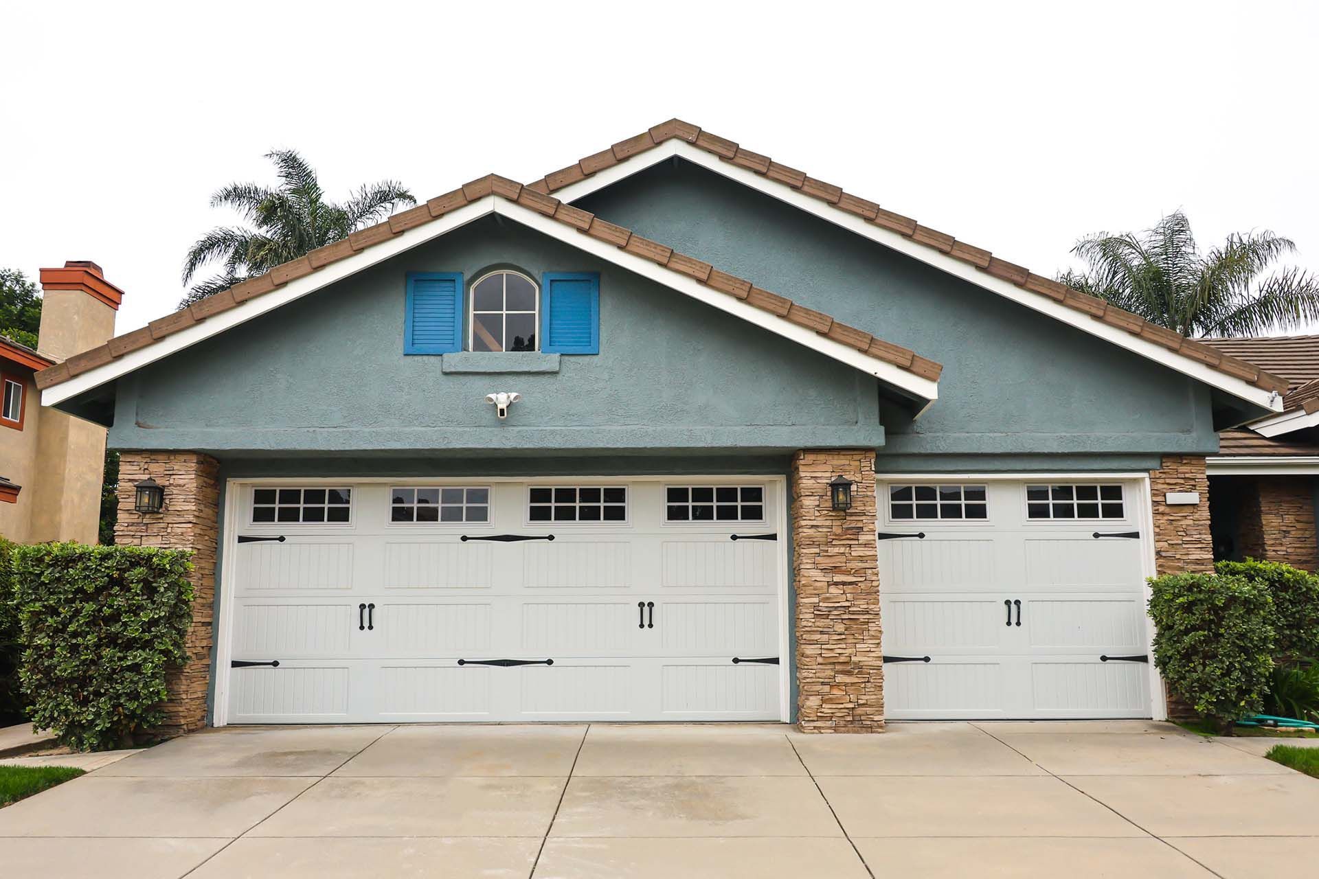 Two-car garage with white doors, blue siding, and a small blue window, under a brown roof.