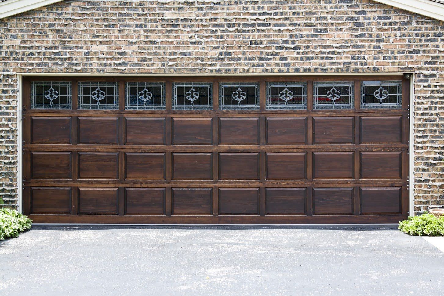 Brown garage door with decorative glass panels set in a brick building.