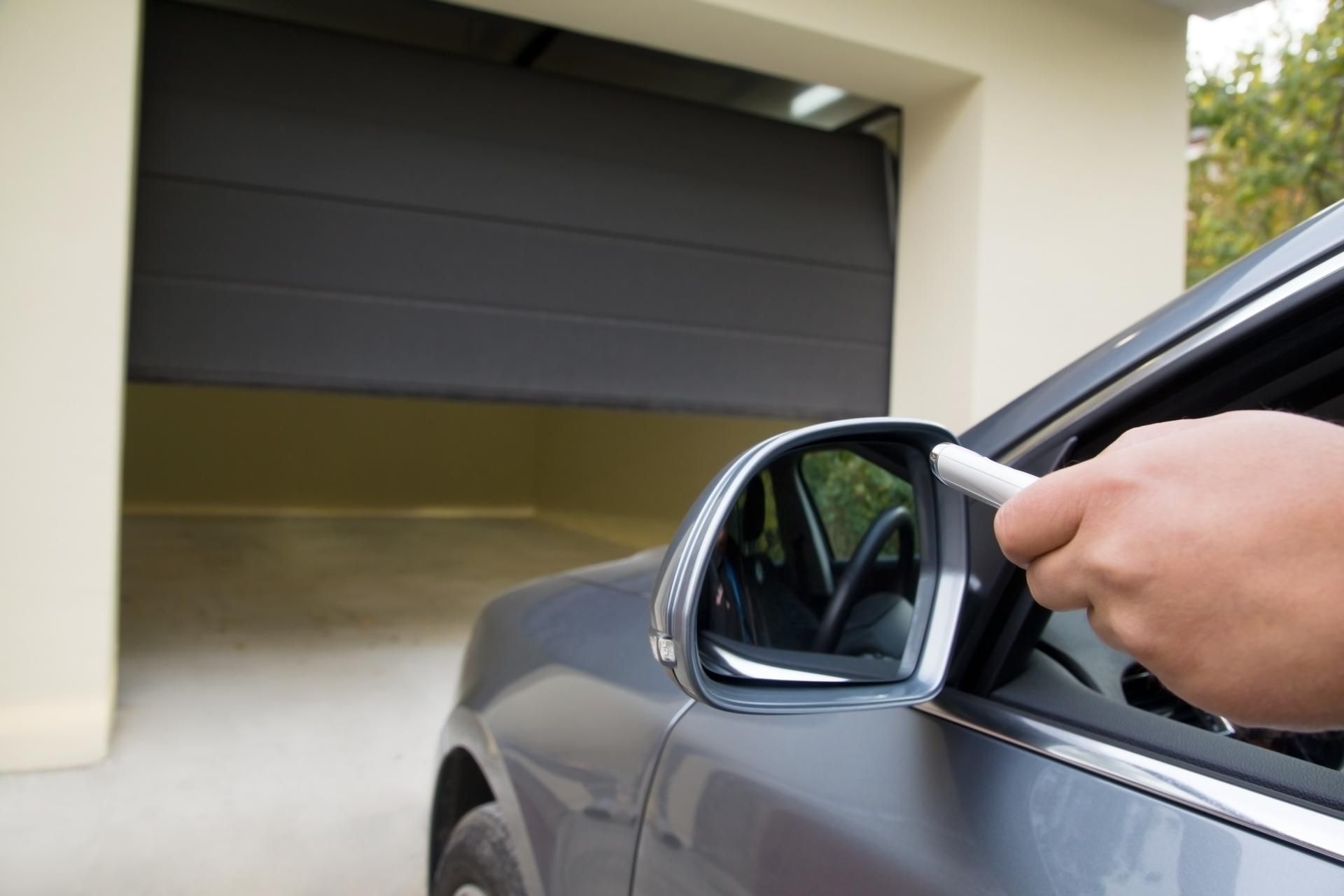 Gray car approaching a garage, using remote to open the garage door.