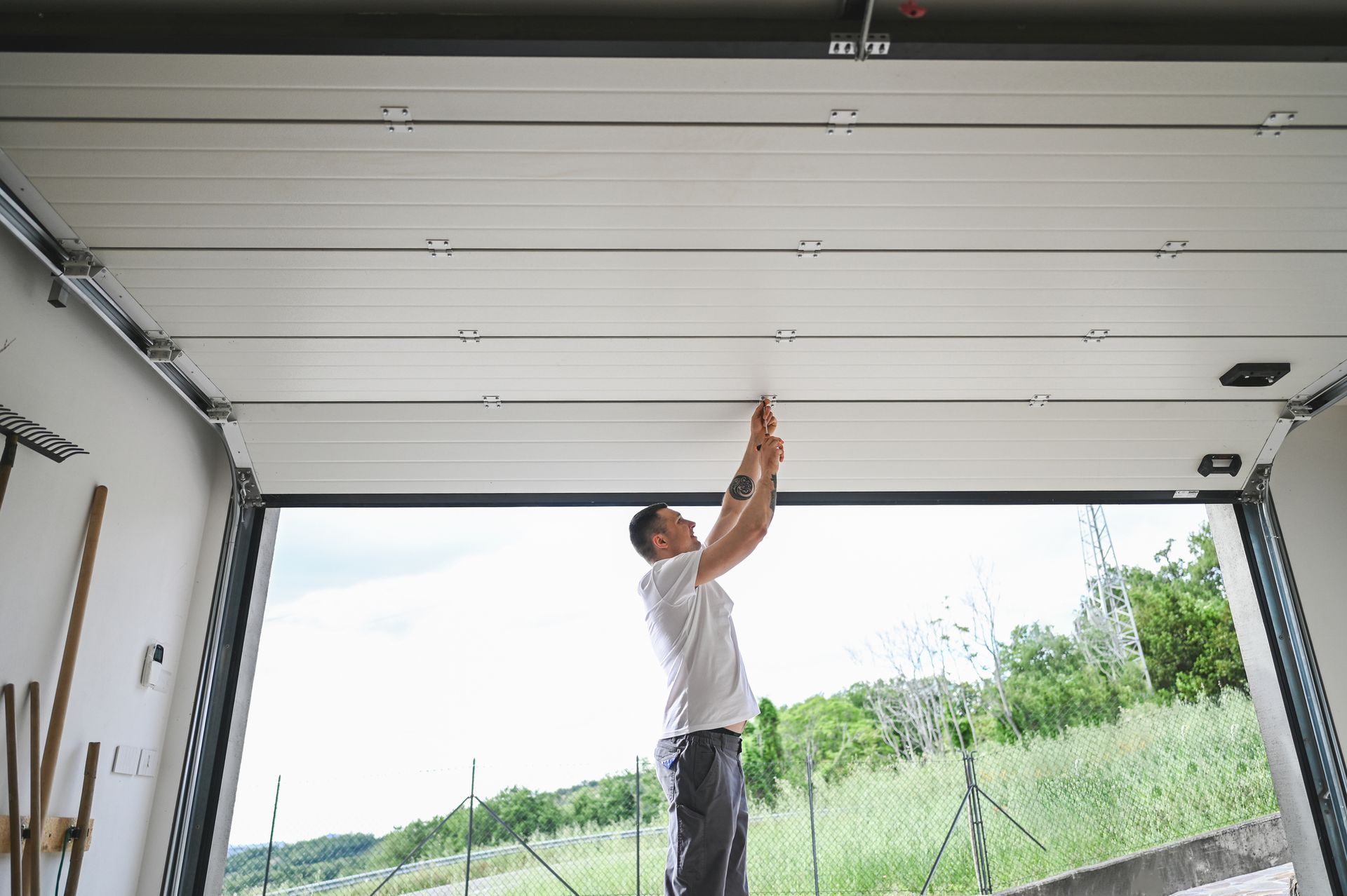 Man inside an open garage, working on the ceiling. Bright outdoors visible.