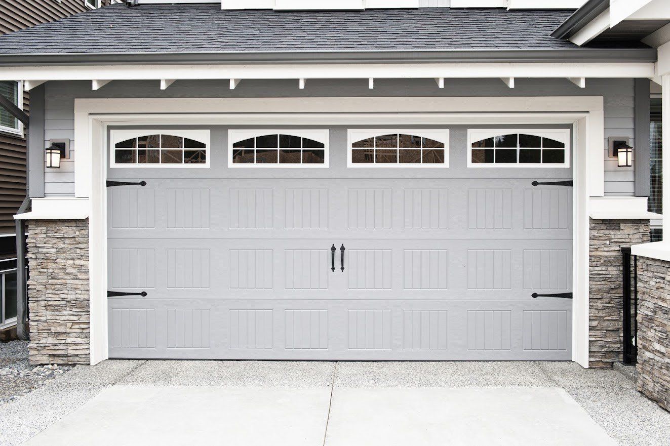 Gray garage door with decorative windows, black hardware, and stone accents.