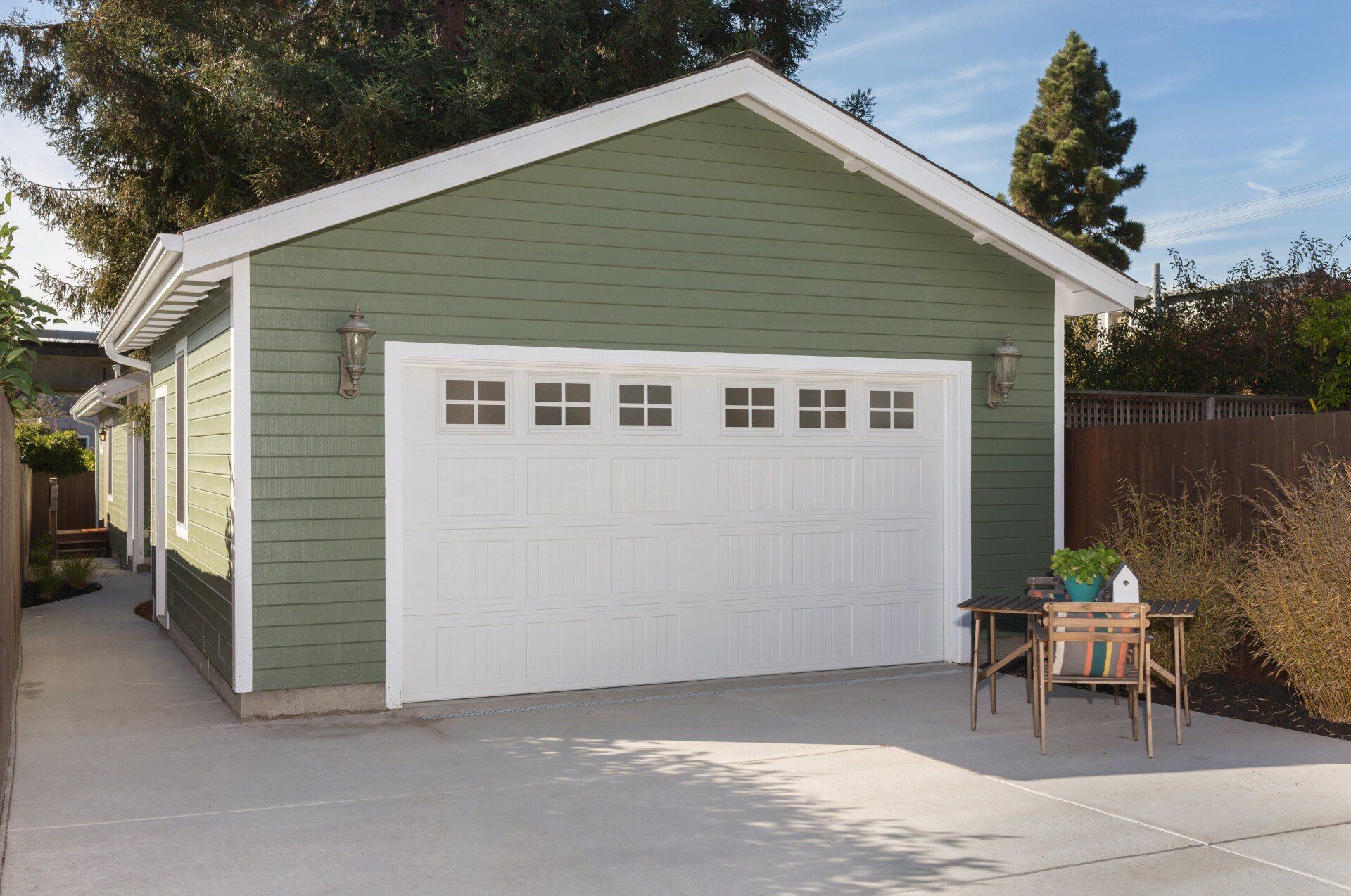 Green garage with white trim and door. A small table sits on the concrete driveway.