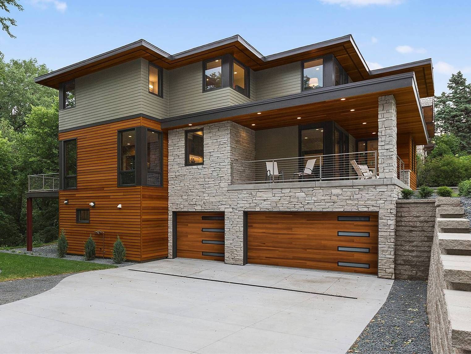 Modern multi-story home with stone and wood exterior, attached garage, and a porch.