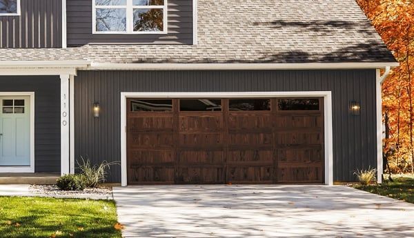 Dark brown garage door on a gray house with a driveway and grass.