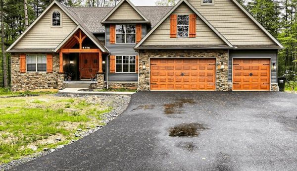 A house with stone accents, a dark gray exterior, and orange garage doors and shutters.