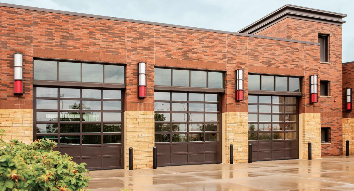 Fire station exterior with red brick, three bay doors, and tan stone accents.