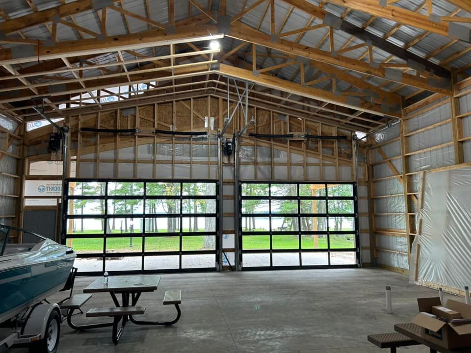 Interior view of an open garage with glass doors, a boat, and picnic table; the structure is unfinished wood.