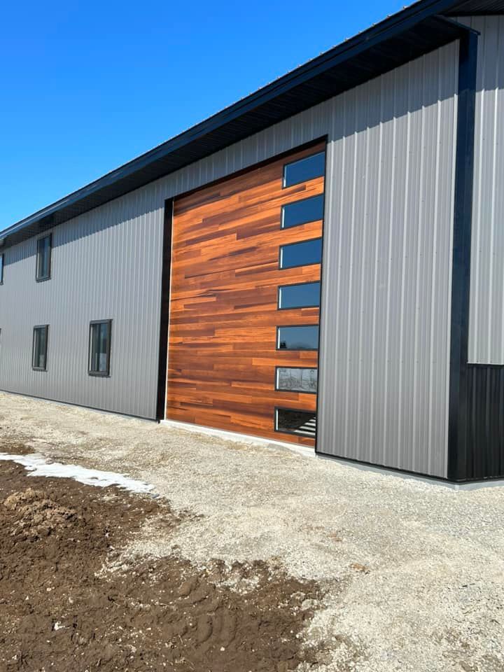 Large wood grain garage door with windows on a gray building under a clear blue sky.