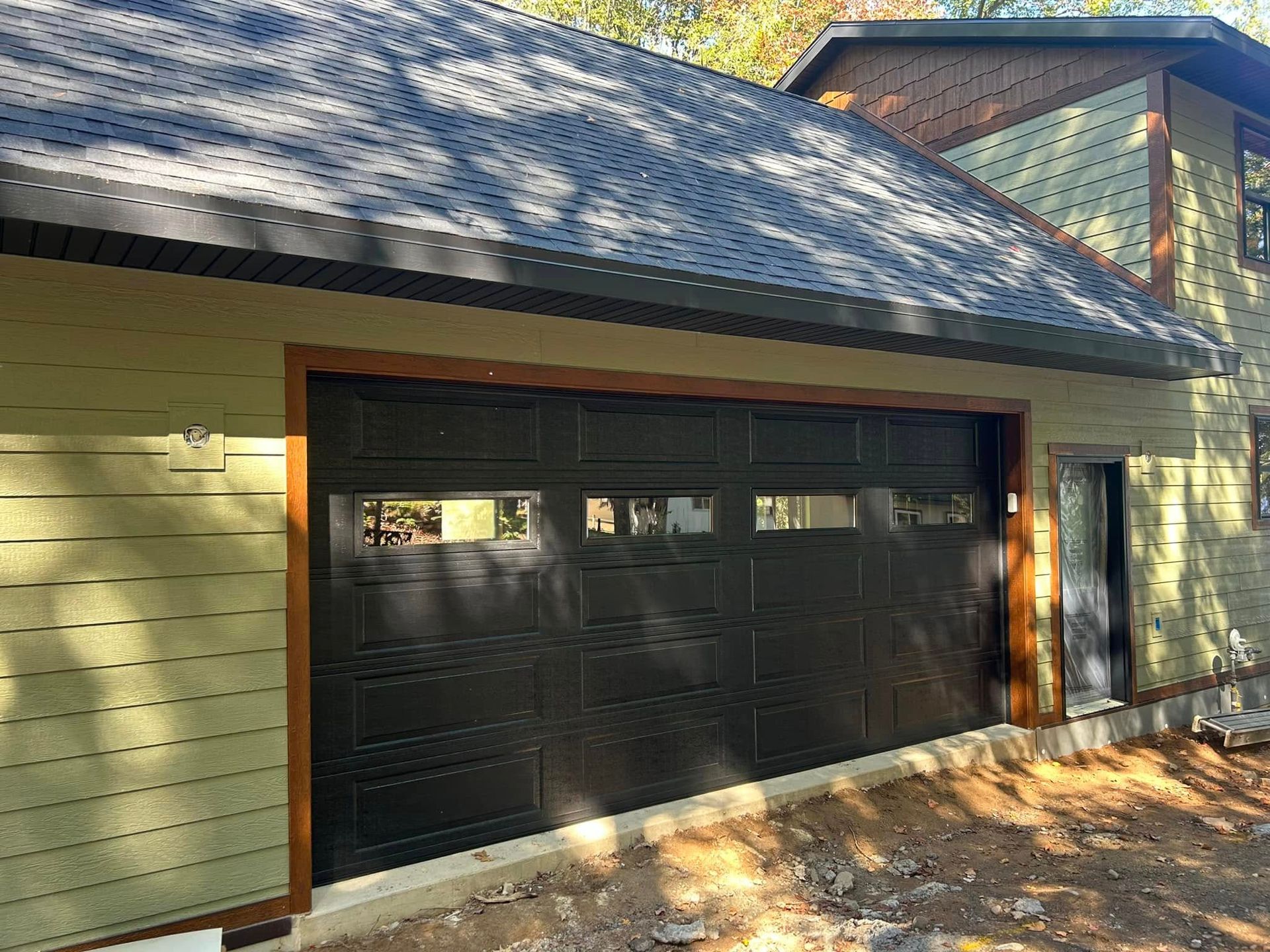 Black garage door with glass panes, wood trim, and green siding on a building.