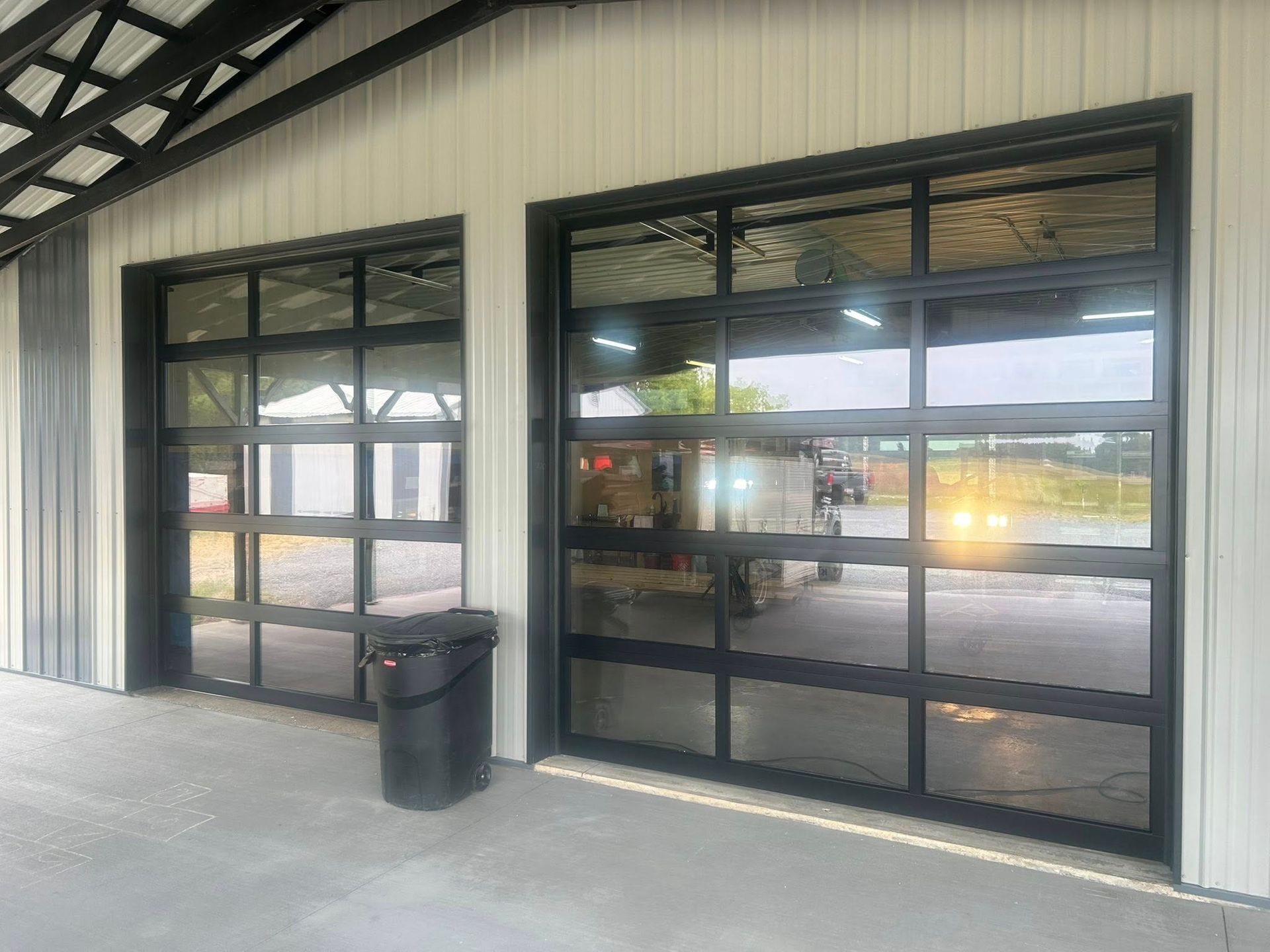 Two glass garage doors with black frames on a metal building, with a trash can in front.