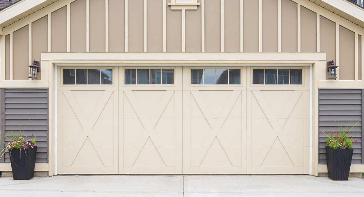 Tan garage door with windows, flanked by planters and lights, against a tan and brown building facade.