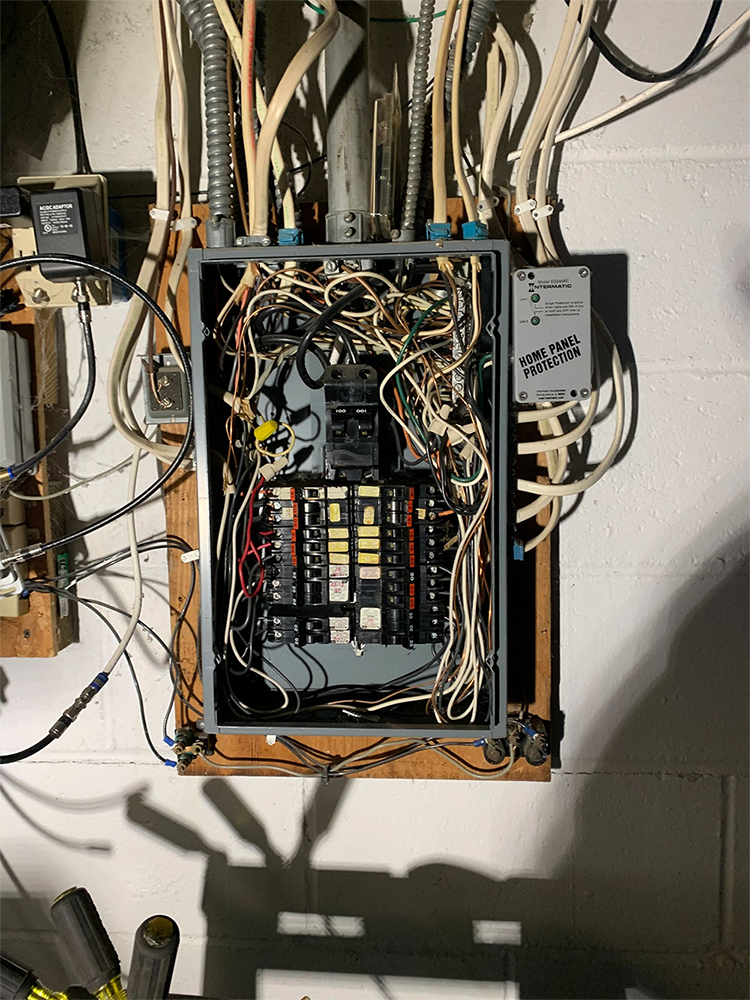 A very messy electrical box is hanging on a wall.