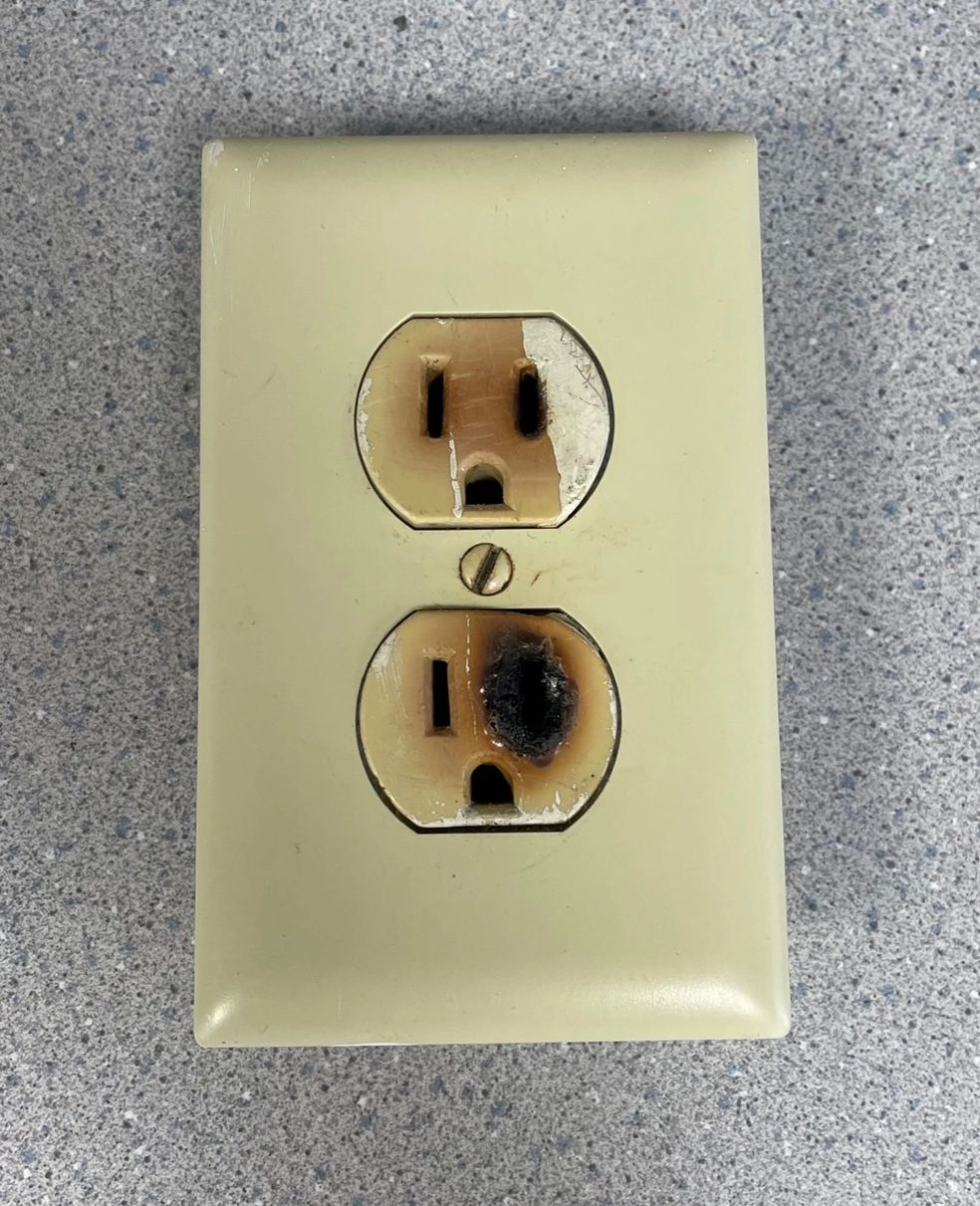 A beige electrical outlet with a burnt and damaged bottom socket.