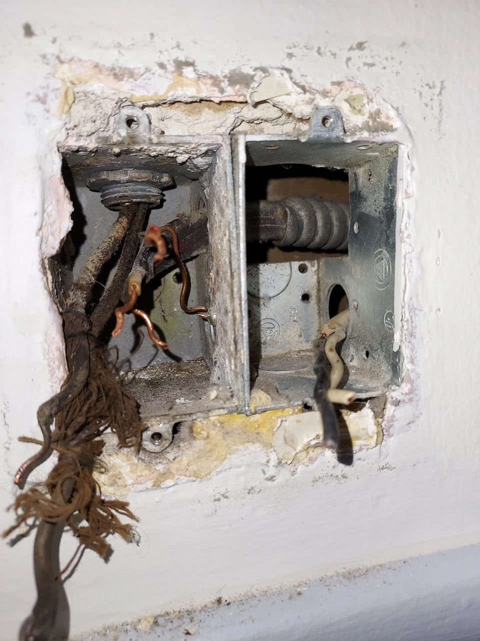 A hole in a wall with wires sticking out of it.