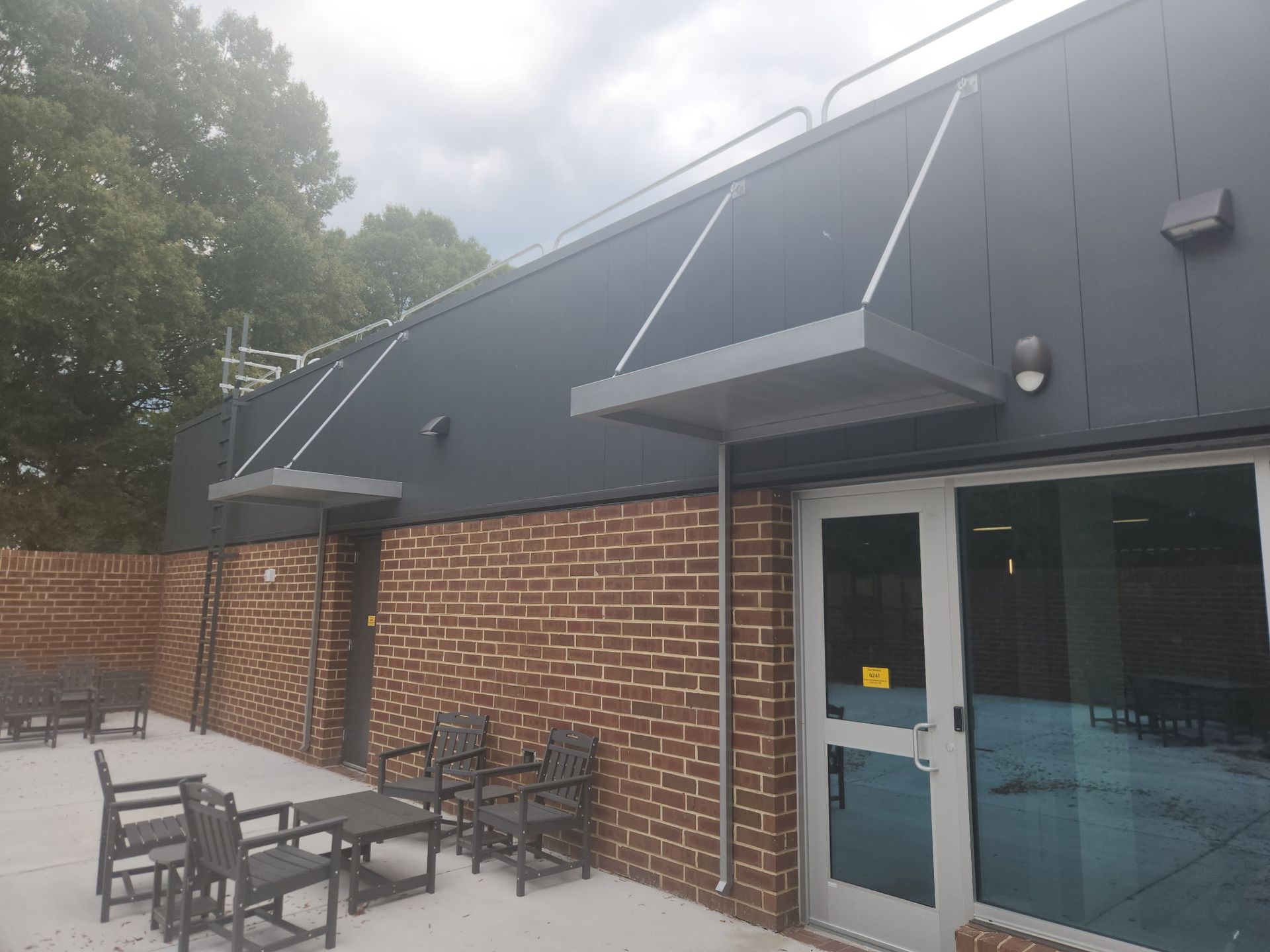 Outdoor patio beside a brick-and-charcoal building with tables, chairs, and glass doors under awnings