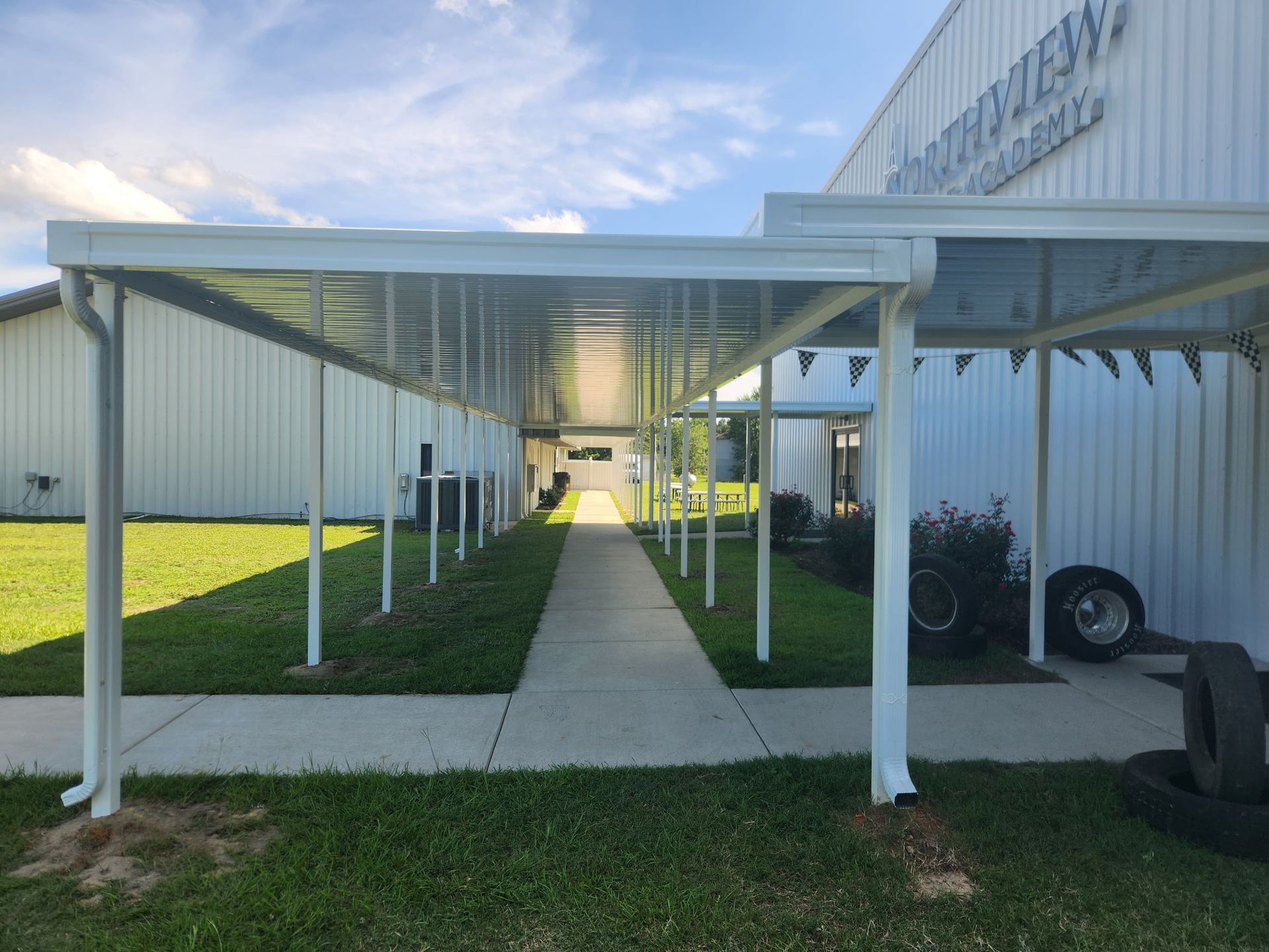 Covered walkway leading to a white building with grassy sides and a concrete path