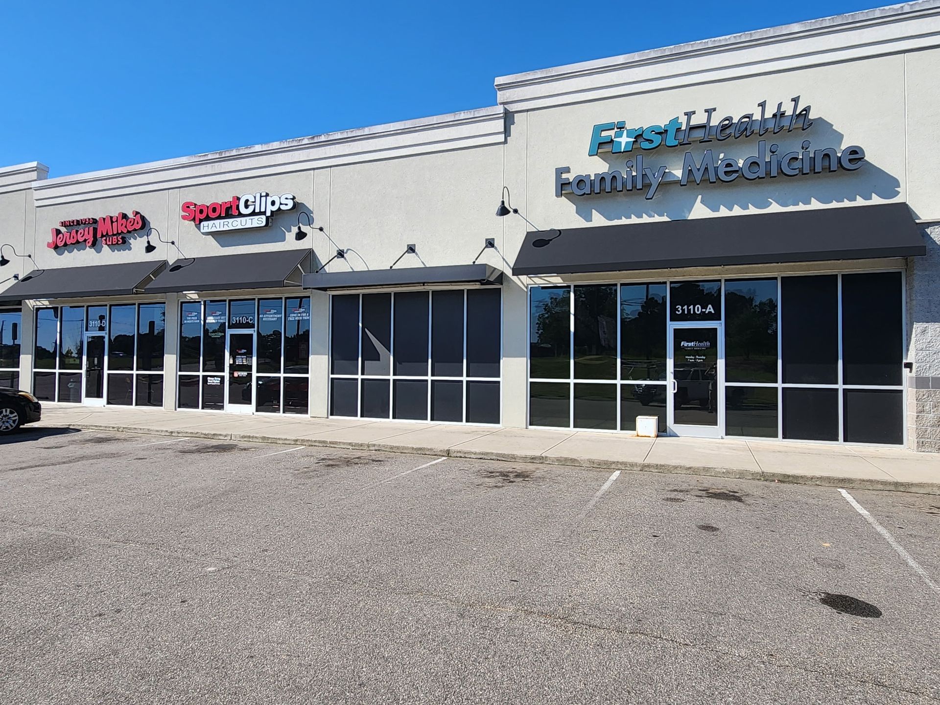 Strip mall storefronts with blue and red signage under a clear sky