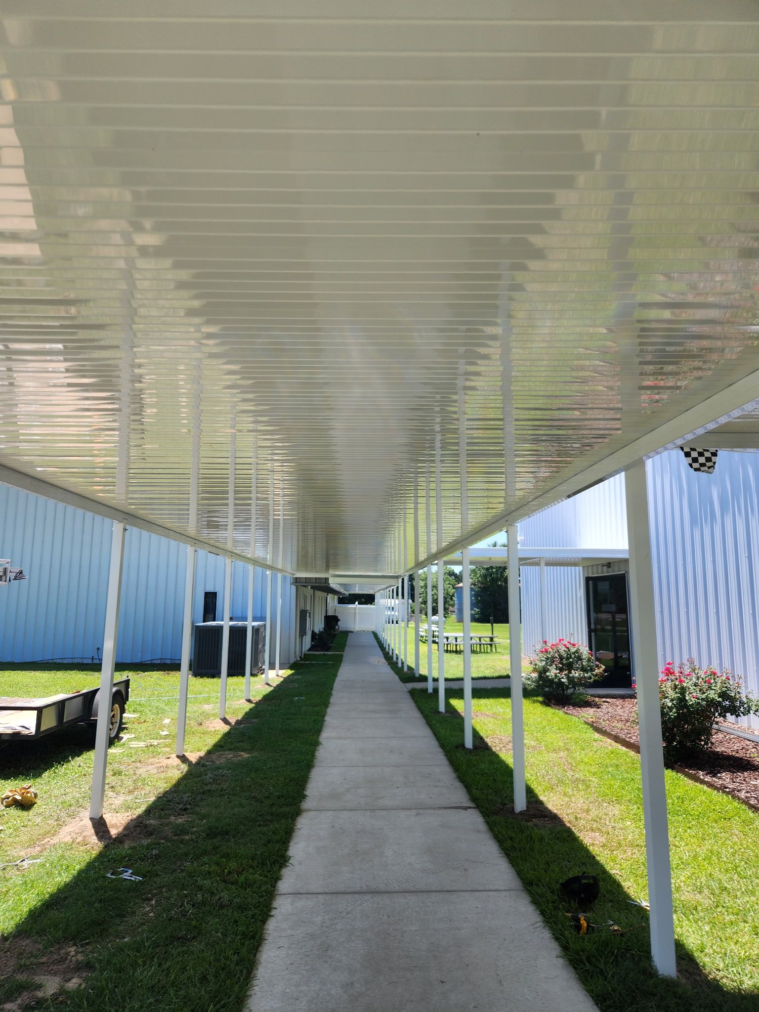 Covered walkway with white columns and roof, leading between blue buildings and landscaped grass
