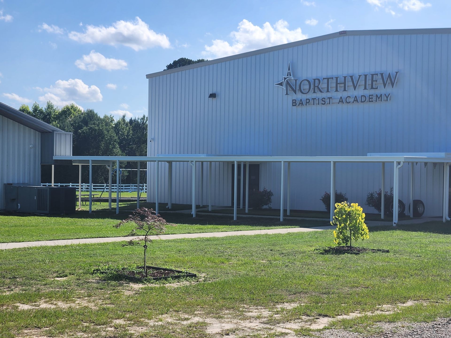 Northview High School building with white exterior, covered walkway, and grassy lawn under a blue sky