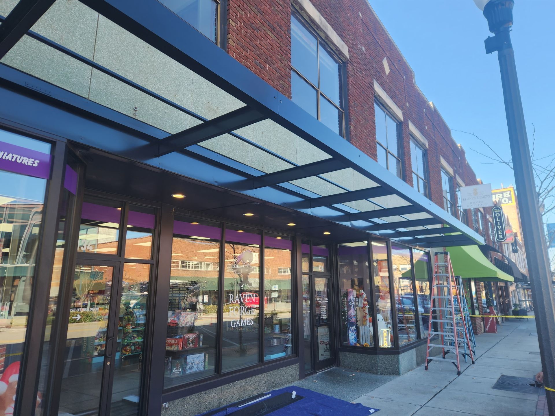 Storefronts with a glass awning along a sunny city sidewalk