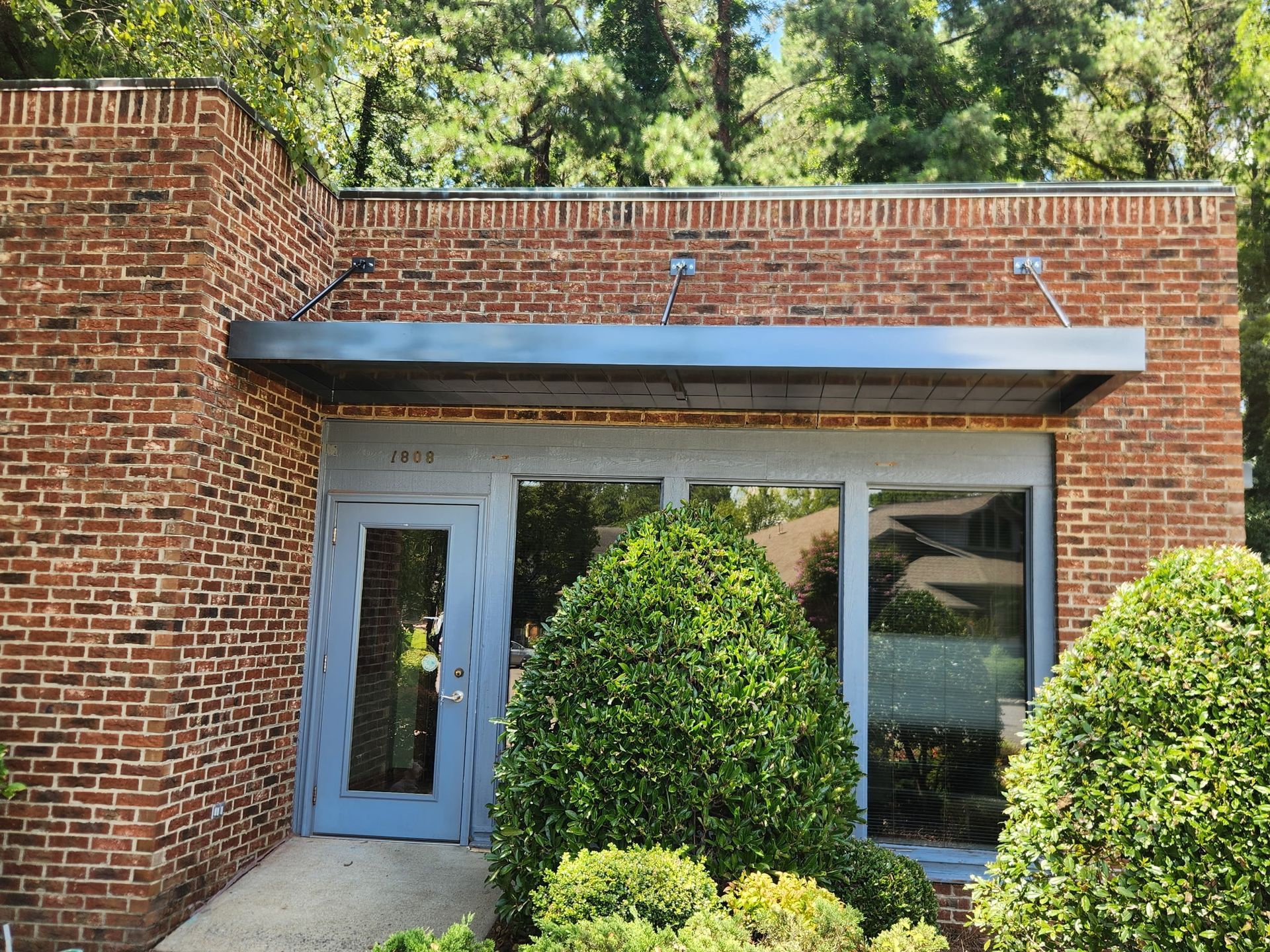 Brick building entrance with a blue door, large window, and green shrubs in front