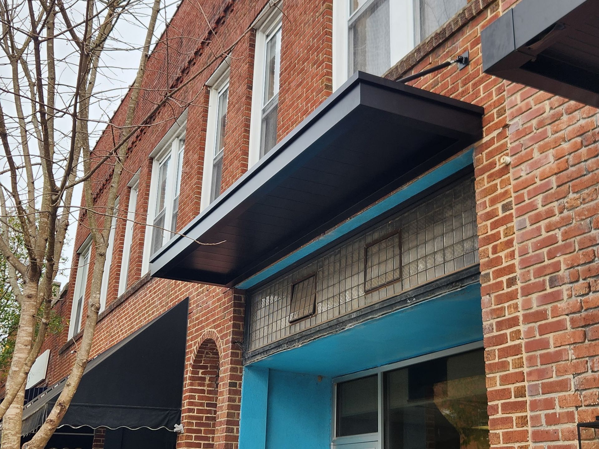 Brick storefront with blue awning and black canopy on a city street