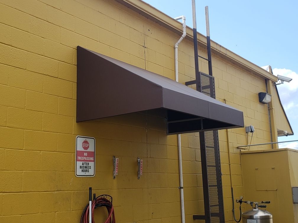 Yellow building wall with a dark brown awning, ladder, and fire safety sign near a doorway