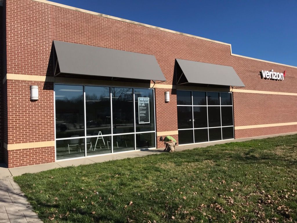 Brick storefront with black awnings, large windows, and a small sign on the right.