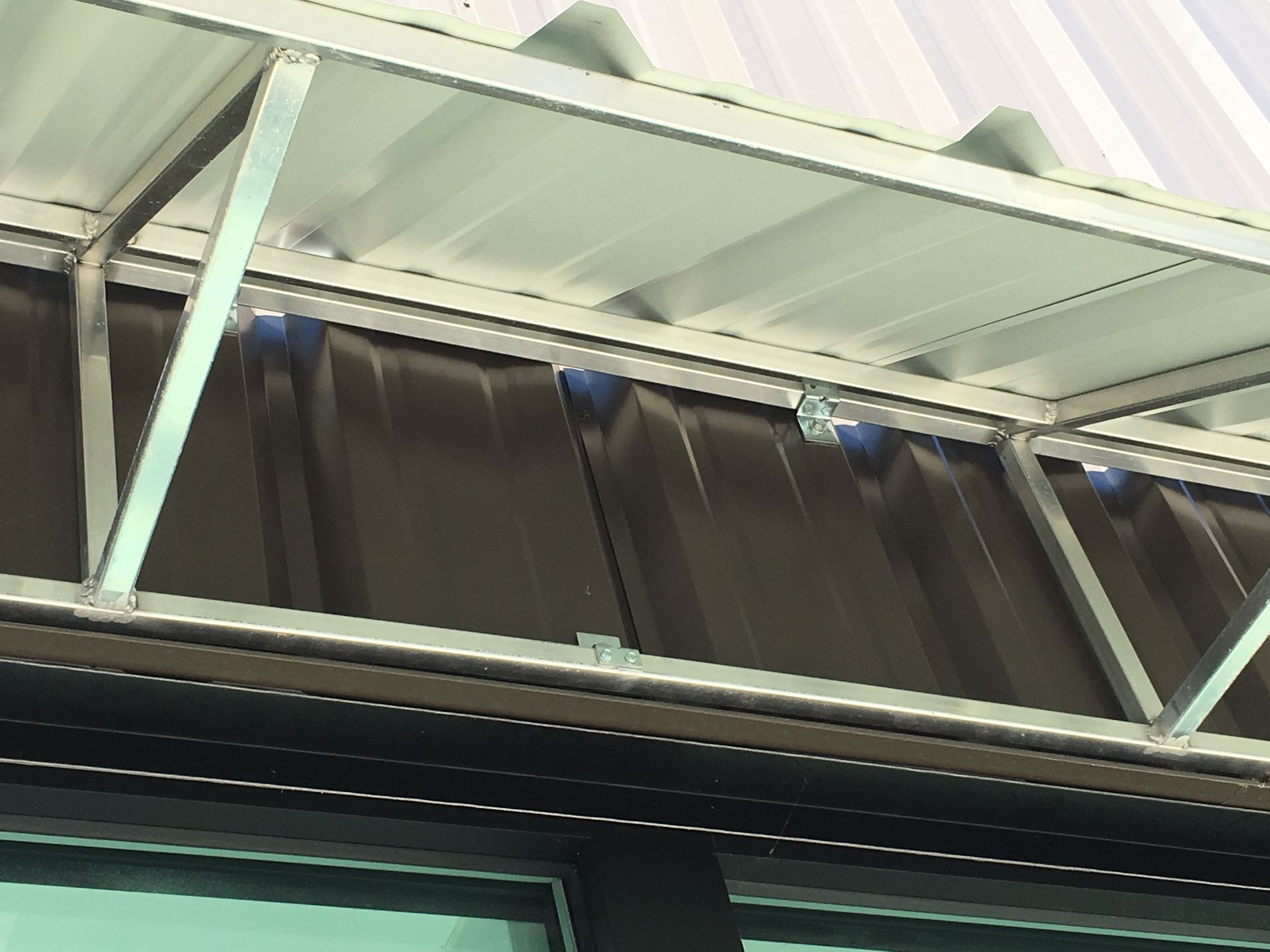 Close-up of a building roof with white beams and dark glass panels under a bright sky